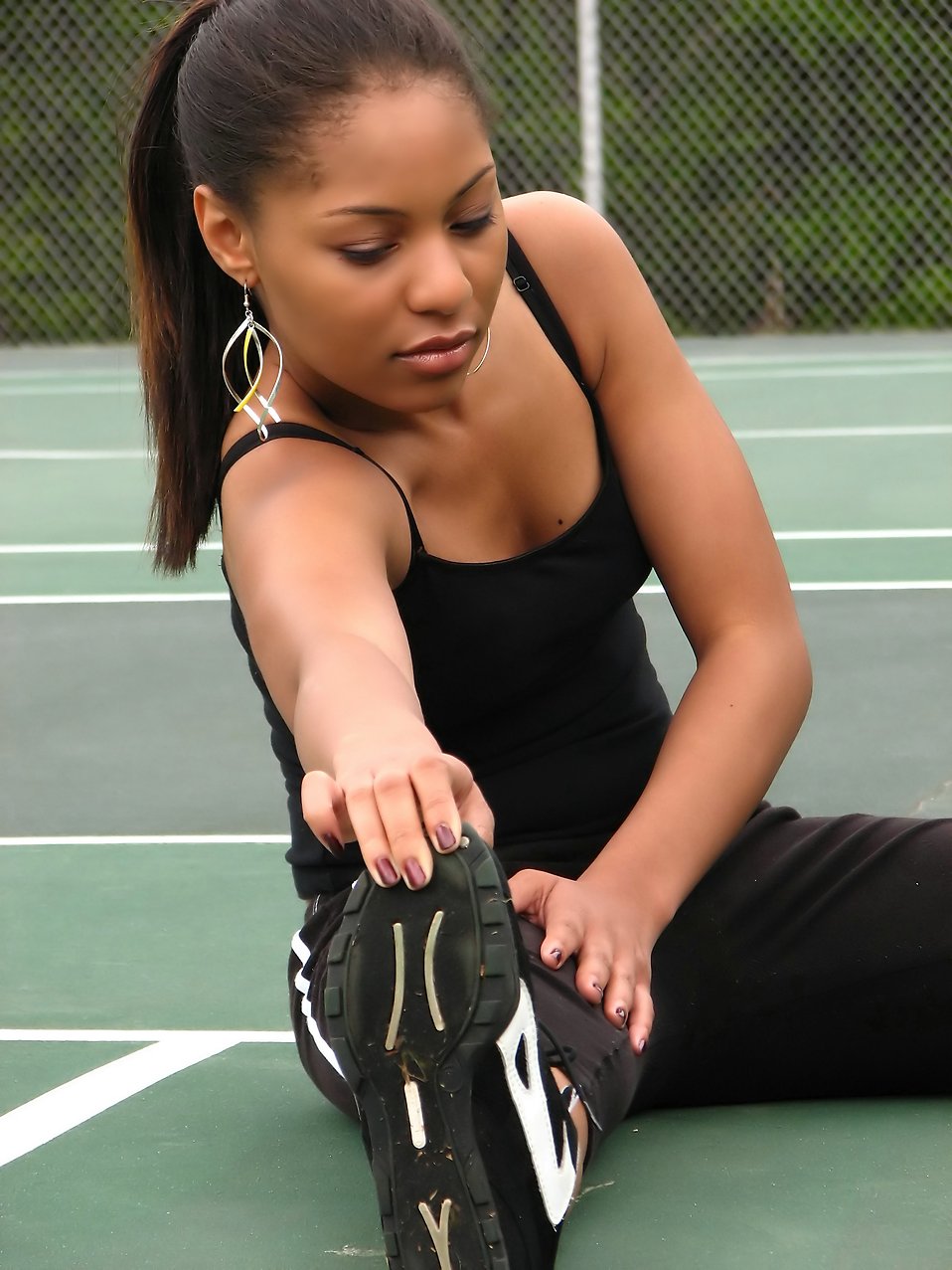 A beautiful African American teen girl stretching on a tennis court : Free Stock Photo