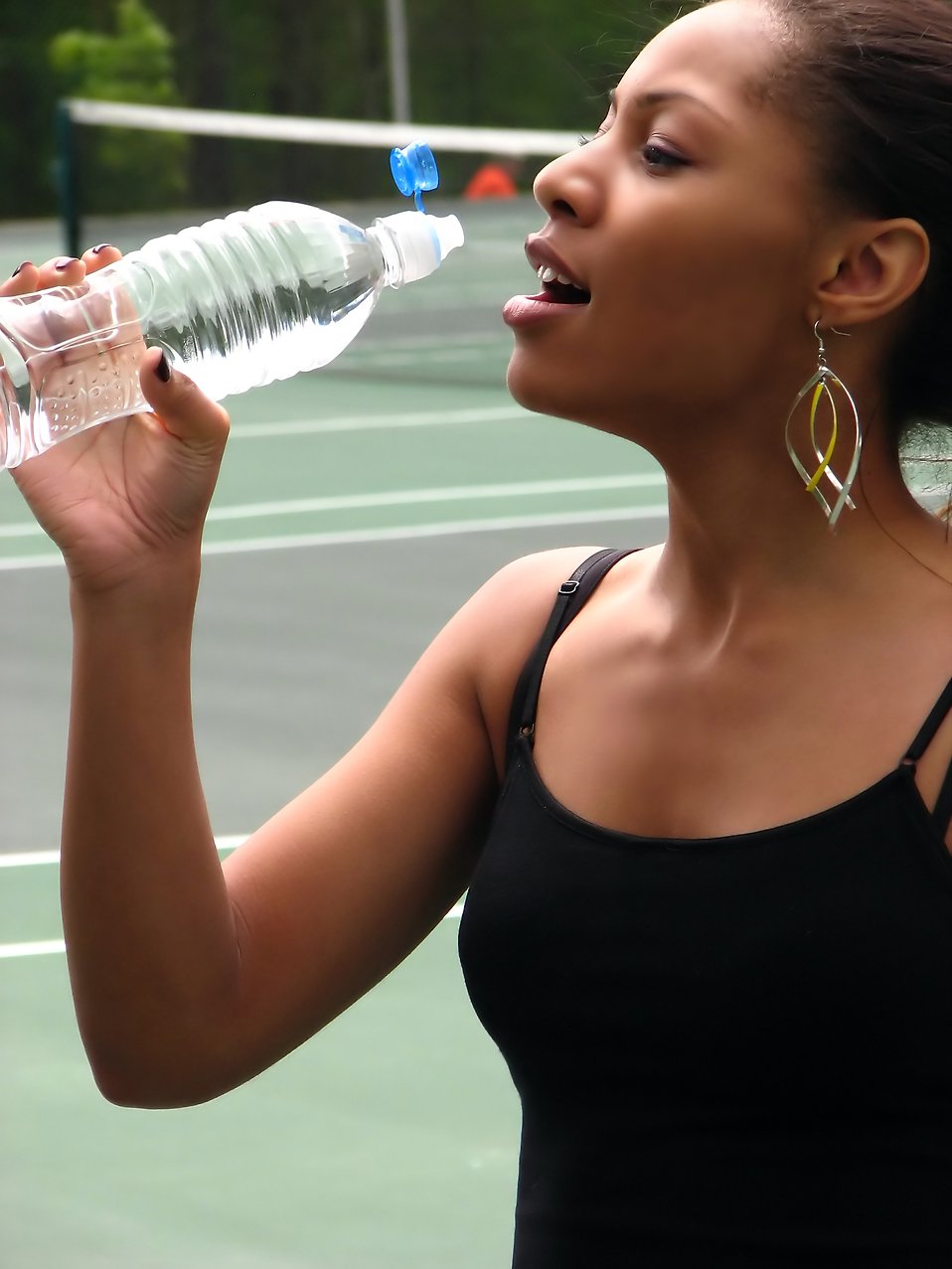 A beautiful teen African American girl drinking water on a tennis court : Free Stock Photo