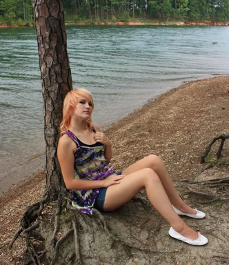 Free Stock Photo: A beautiful young woman posing against a tree by a lake