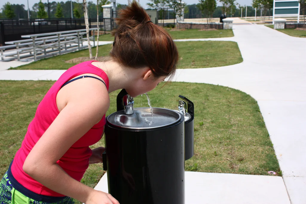 A young girl drinking from a water fountain in a park : Free Stock Photo