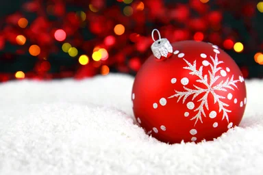 Free Stock Photo: A red Christmas ornament in the snow with lights in the background