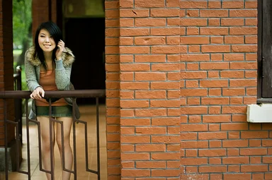 Free Stock Photo: A beautiful Chinese girl posing on a railing by a brick wall