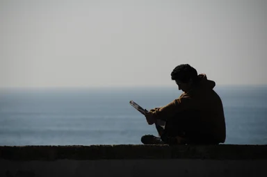 Free Stock Photo: Silhouette of a man reading by the ocean