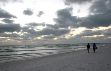 Free Stock Photo: A couple walking on the beach under a cloudy sunset